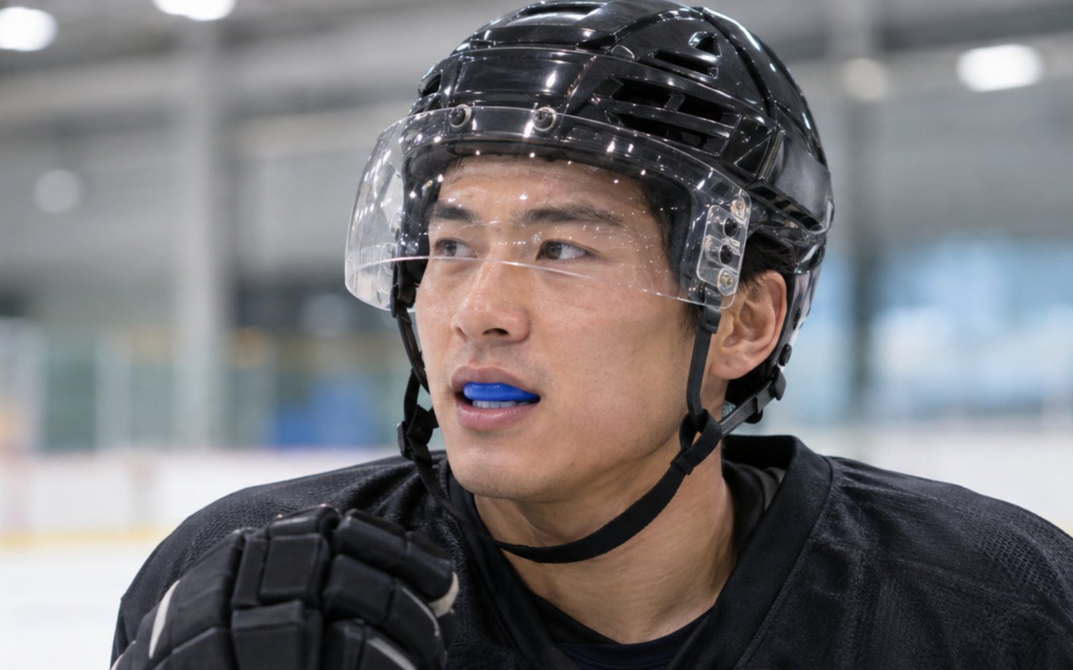 A hockey player in a helmet and visor wearing a blue mouthguard