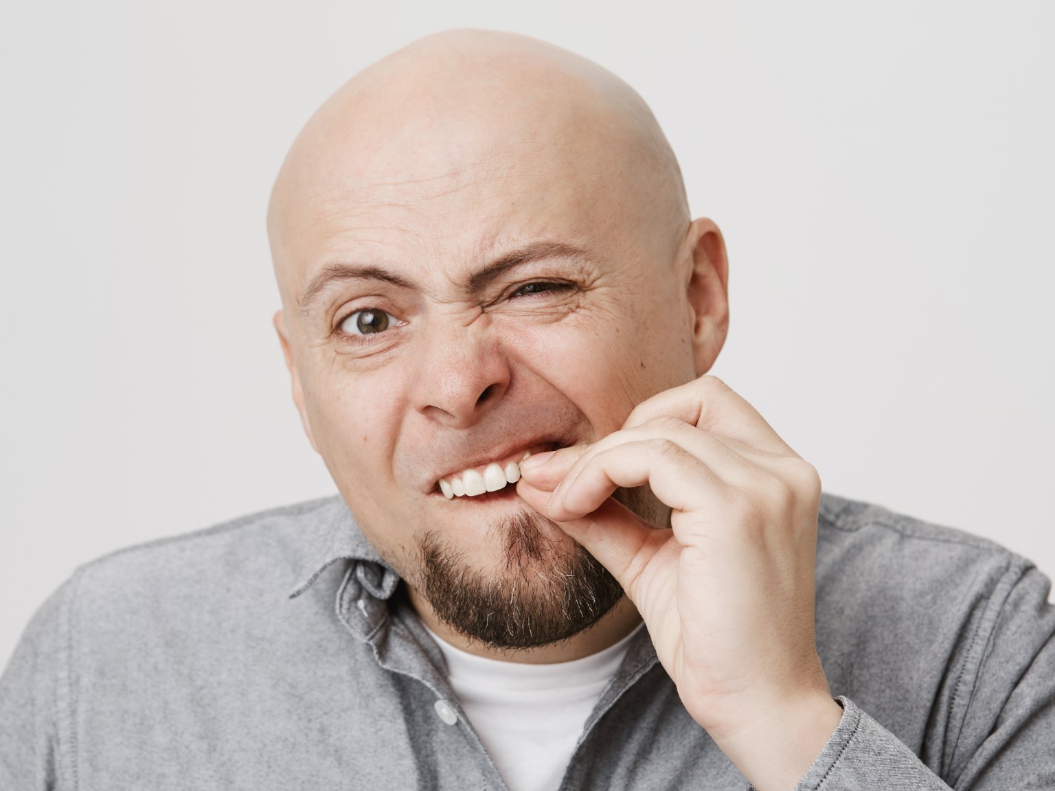A man wincing as he pinches one of his front teeth between finger and thumb to test if it moves