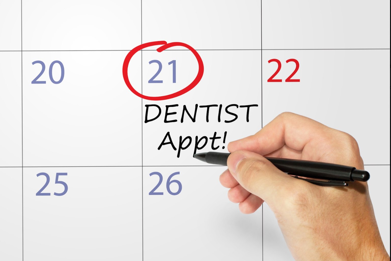 A hand writing 'Dentist Appt!' under a circled date on a wall calendar