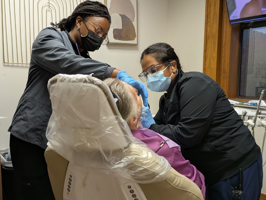 Two assistants leaning in to treat an older patient in the chair