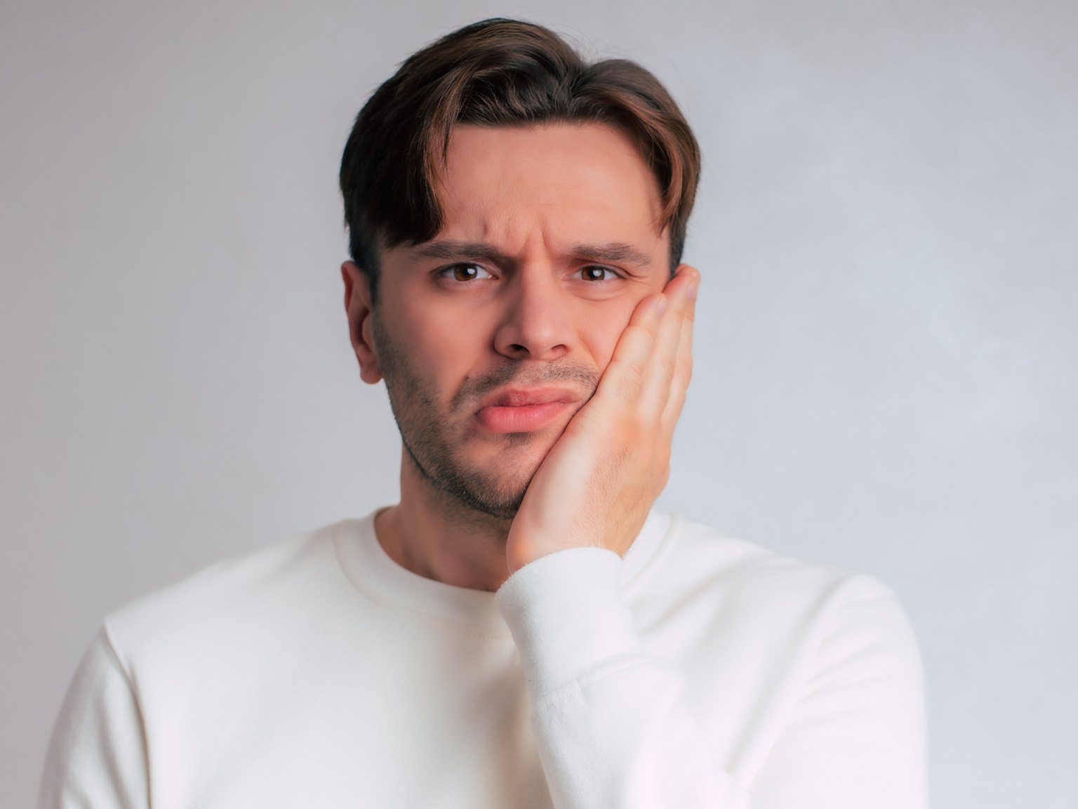 A man frowning and pressing his palm to a tender cheek