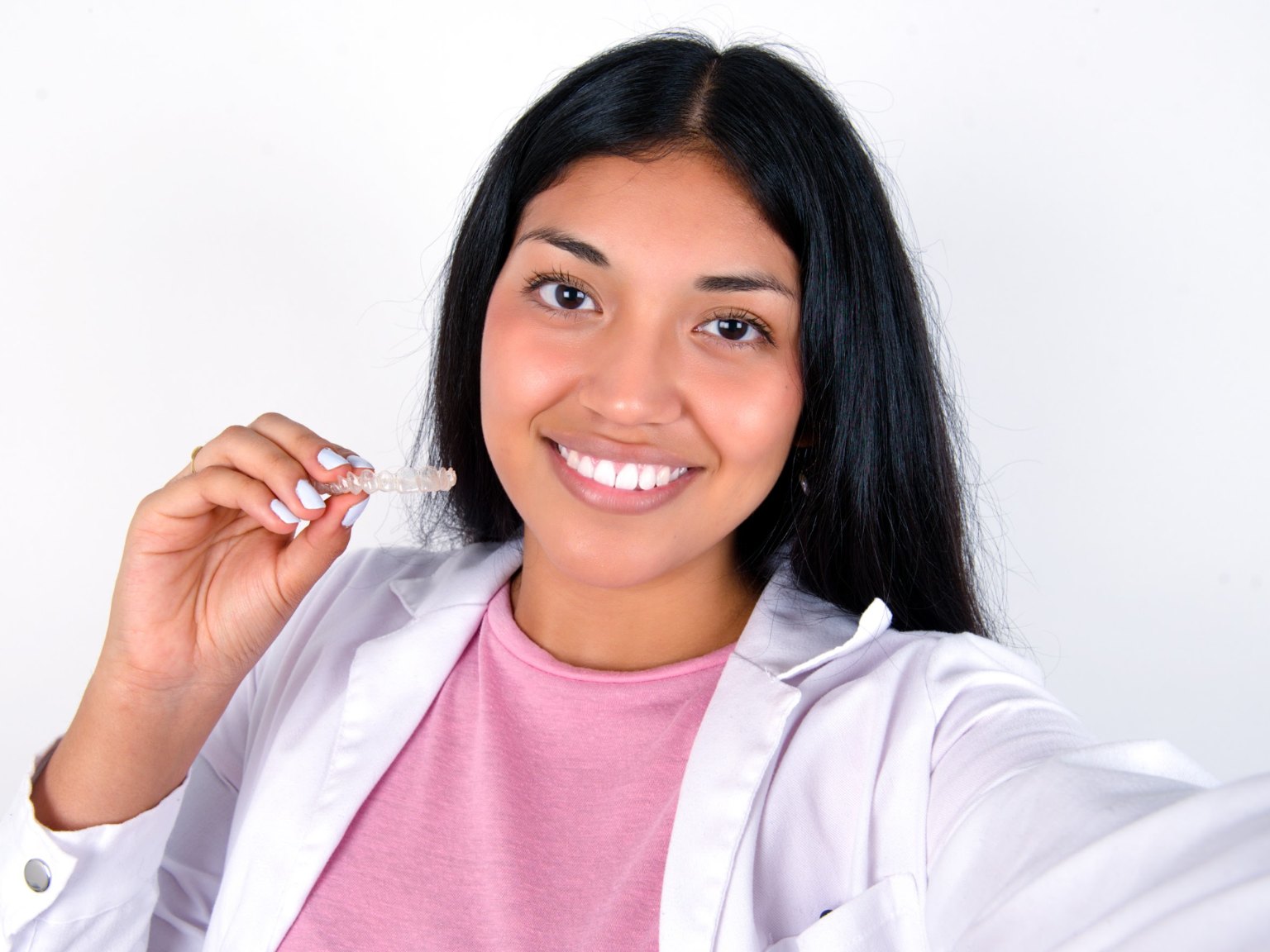 A smiling young woman holding up a clear aligner tray