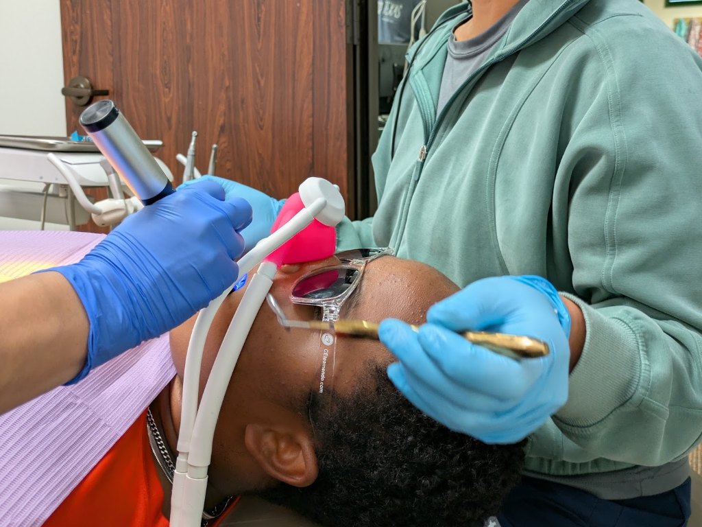 A patient reclined with a nitrous oxide nose mask while the dentist works in loupes