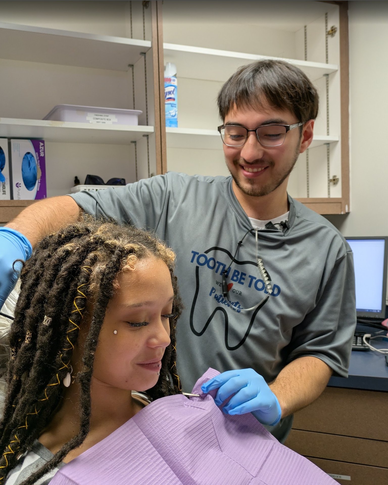 An assistant clipping a bib on a smiling patient in the chair