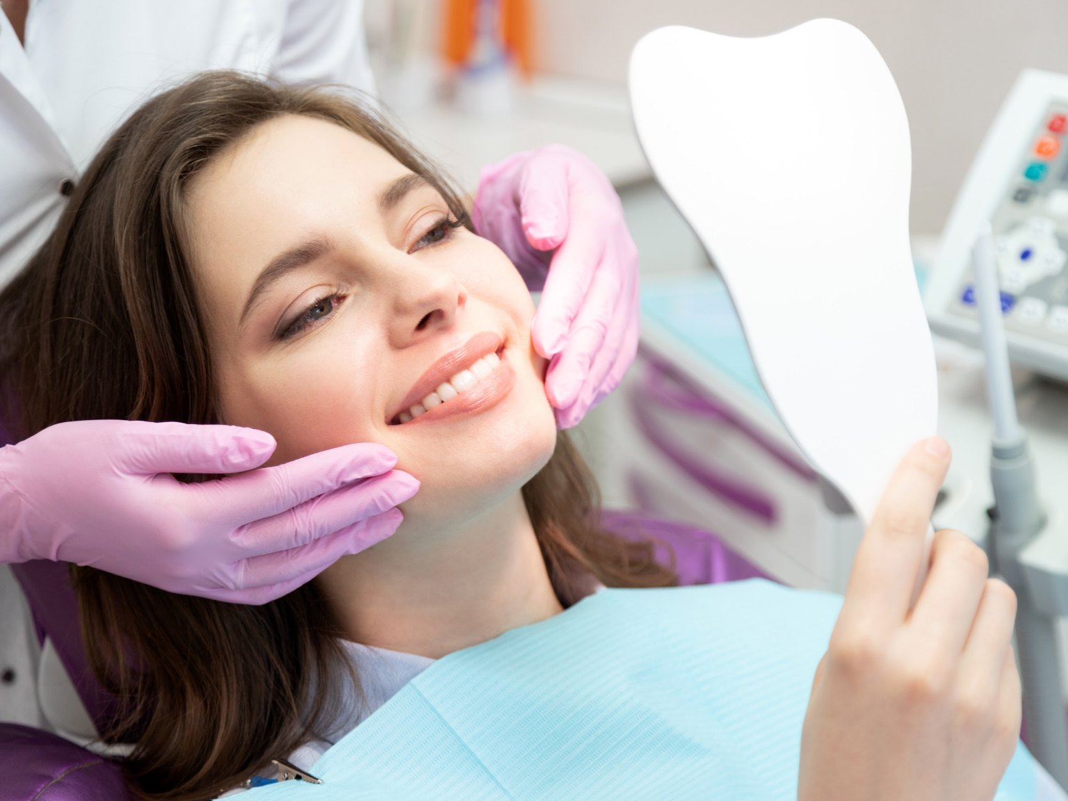 A woman in the dental chair smiling at her new smile in a hand mirror