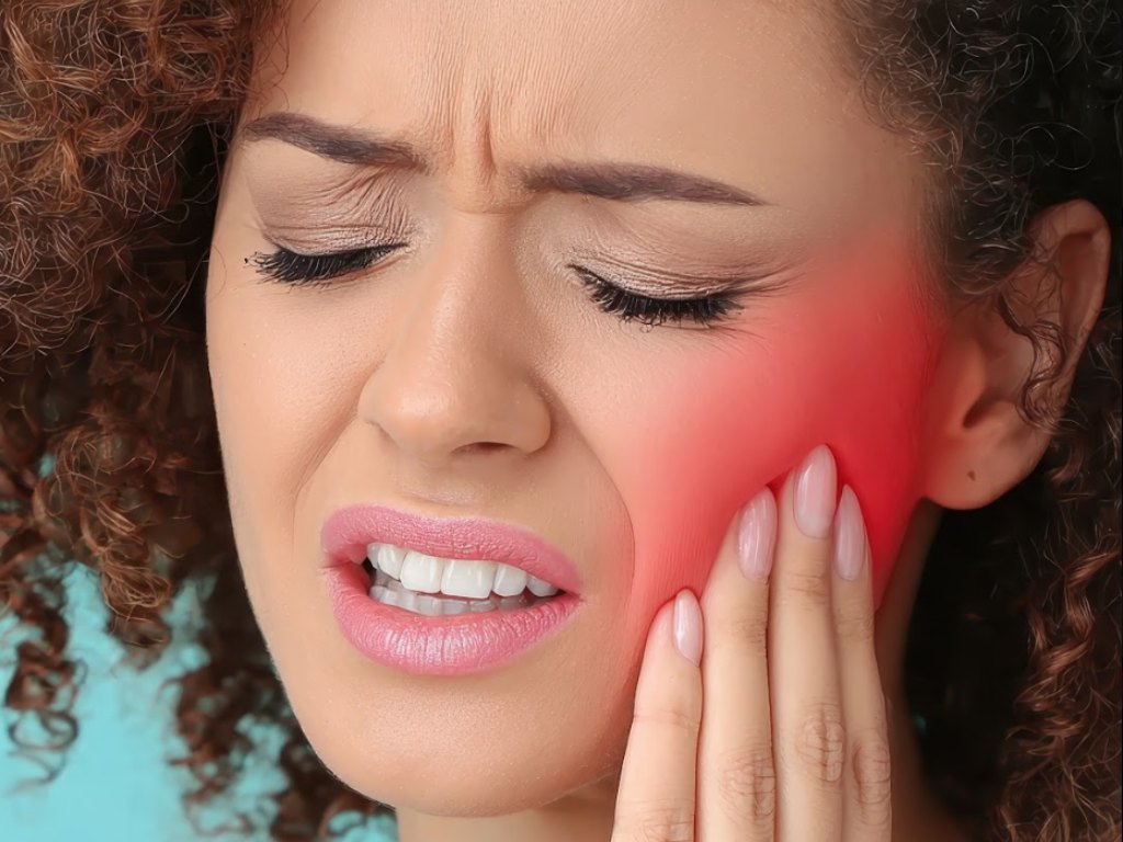 A woman wincing with her hand on her aching jaw