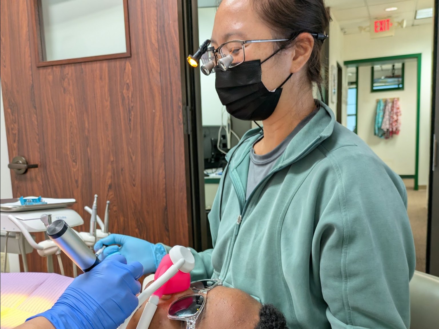 A dentist in loupes treating a reclined patient in protective glasses