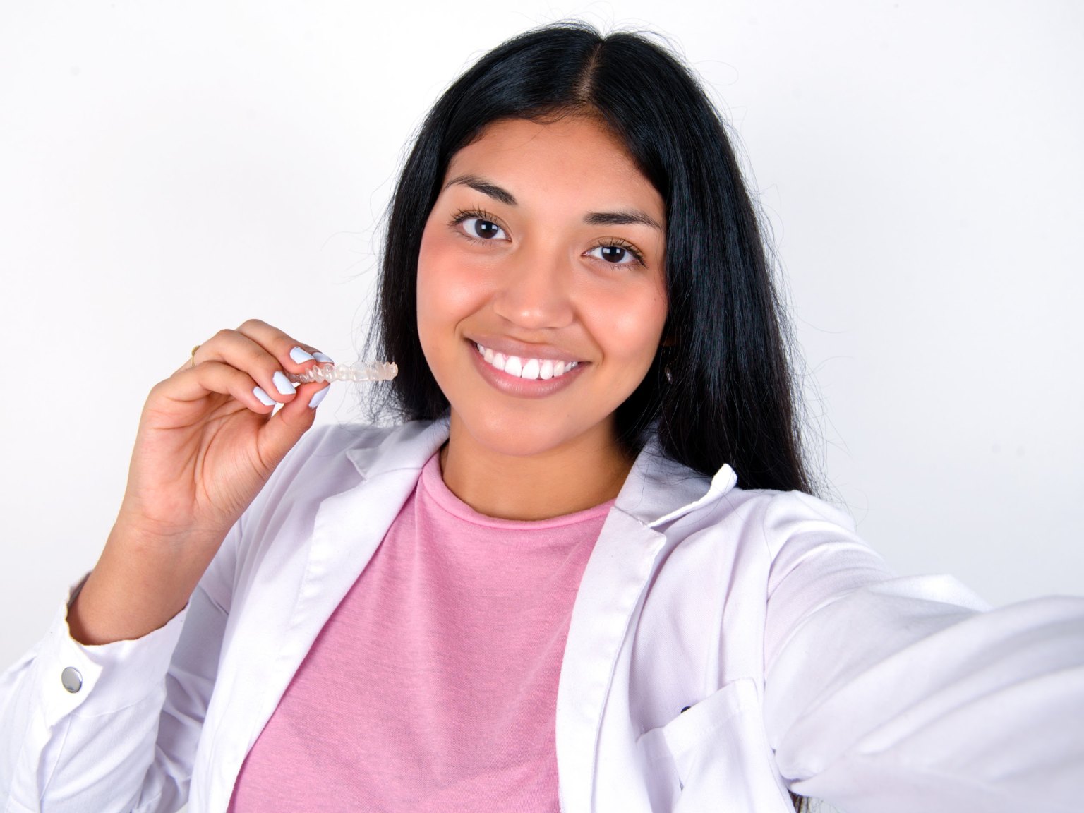 A smiling woman holding up a clear aligner tray